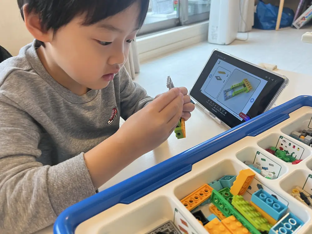 教室でブロックを組み立て、タブレットでプログラミングする子どもたちの様子