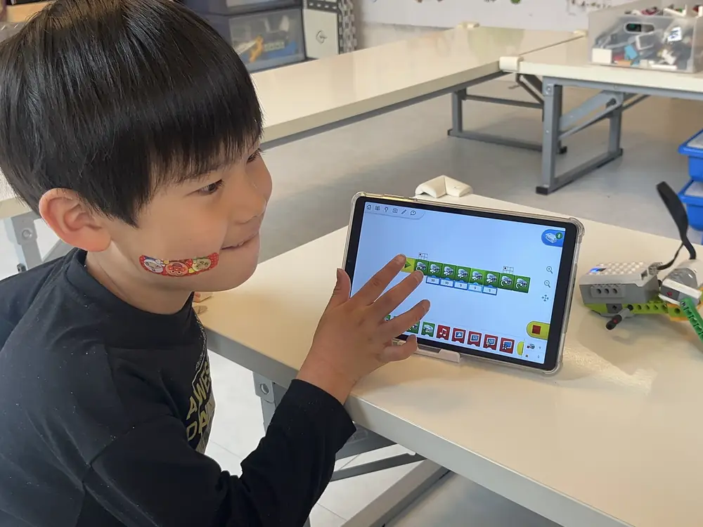 教室でブロックを組み立て、タブレットでプログラミングする子どもたちの様子